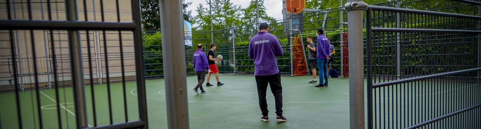 Le city-stade d'un quartier, vu à travers la grille, un médiateur au milieu des jeunes